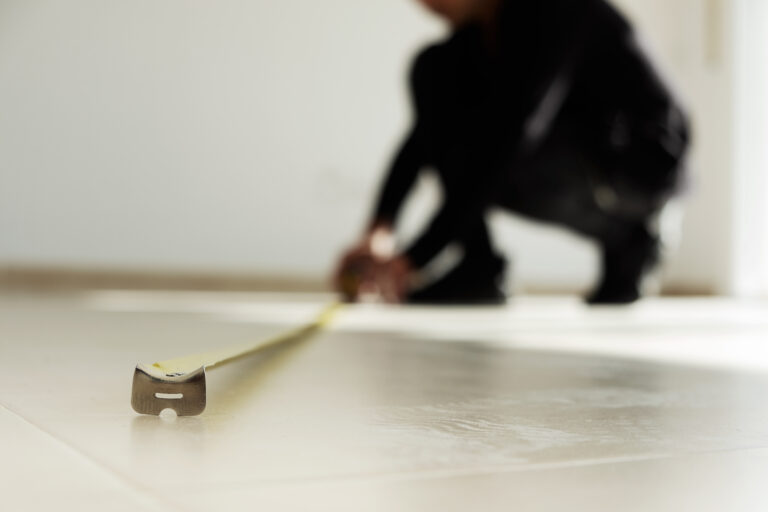closeup of a young caucasian man using a measuring tape on a beige tiled floor